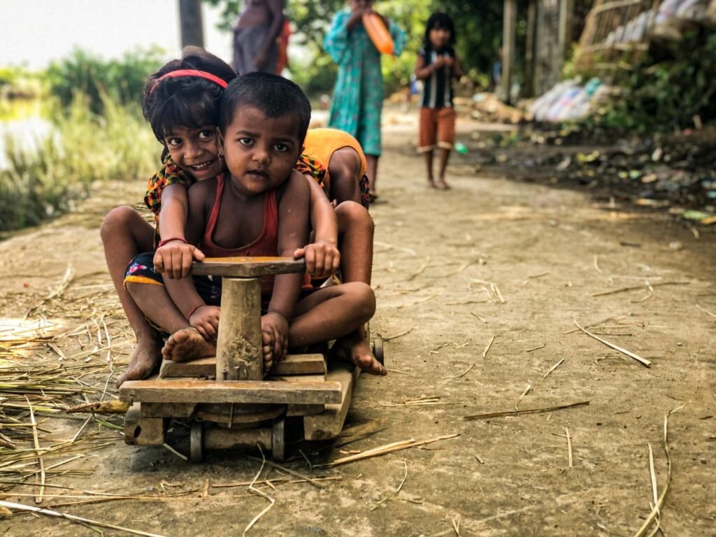Young children joyfully ride a homemade wooden toy cart in an outdoor setting, showcasing playful innocence and camaraderie.