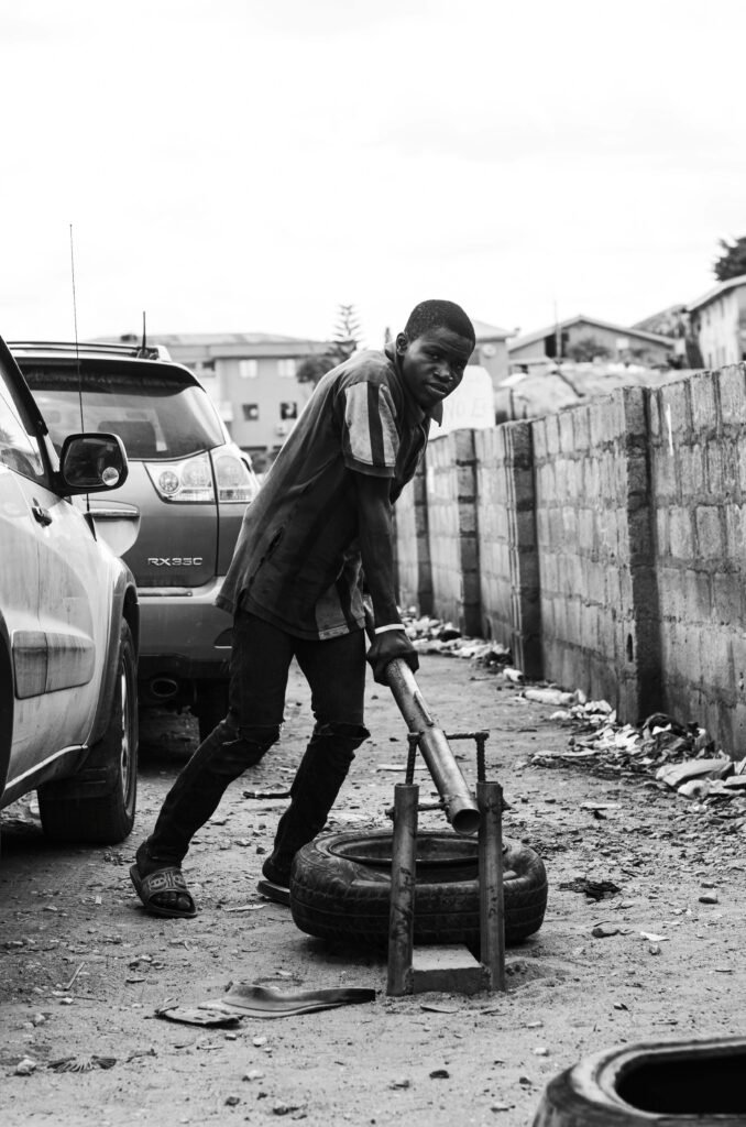 Black and white photo of a street vulcanizer repairing a tire in a busy urban area.